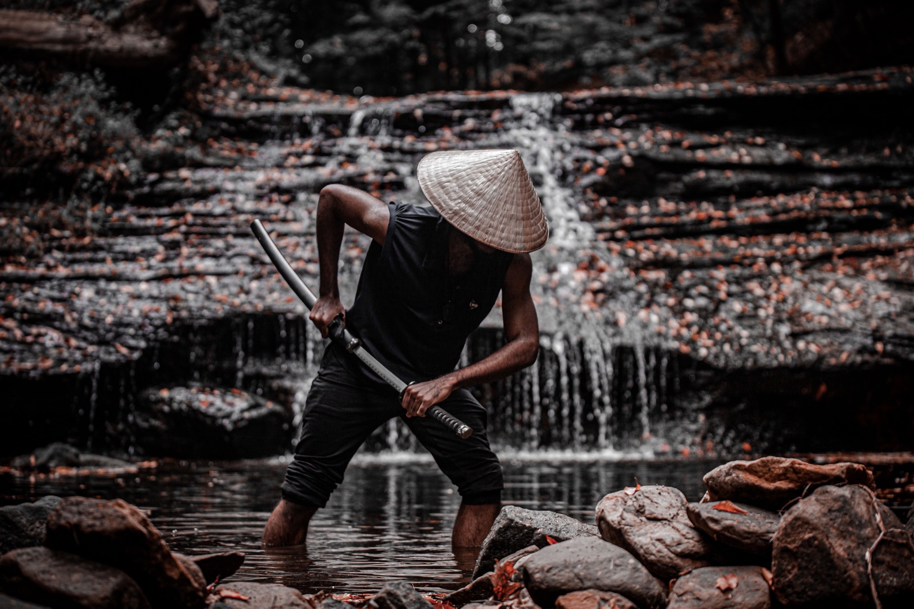 Figura con cappello conico che impugna una spada in un paesaggio d'acqua e pietra